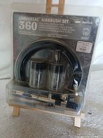 Front view of sealed Badger Universal 360 airbrush set showing airbrush, hose, jars