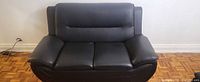 Front view of black faux leather loveseat showing two seat cushions, back cushion, rolled arms
