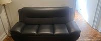Front view of black faux leather three-seat sofa