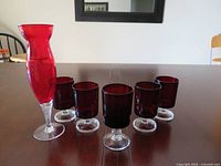 Vase and six cranberry red glasses on table