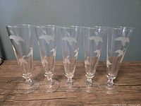 Front view of five etched duck pilsner glasses standing in a row