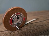 Brown leather-textured round tape measure with metal winding handle shown on wood surface