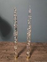 Front view of two clear Lucite candles with silver flakes and gold-tone caps