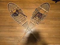 Pair of crossed wooden snowshoes on floor showing overall condition