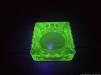 Square uranium glass ashtray glowing under UV light, top view