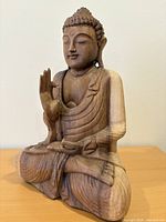 Front left view of seated wooden Buddha on table