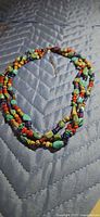 Full view of triple-strand multicolour beaded necklace on quilted surface