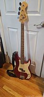 Full view of red Squier P-Bass guitar with strap leaning against door