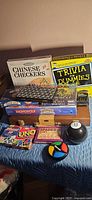 Group shot of all boxed games, card decks and Magic 8 Ball on quilted surface