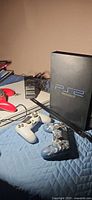 PS2 console lying on quilt with two controllers and cables