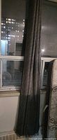 Full length view of single dark gray curtain hanging beside window