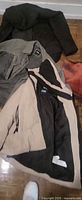 Three jackets on floor: black puffer, grey jacket, beige/black jacket