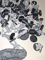 Pile of grey plastic miniatures with black round bases and scenic base visible