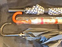 Three umbrellas laid horizontally: gingham, clear plastic, black