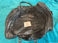 Top view of empty black vinyl weekender bag showing handles and brass hardware
