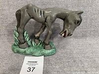 Full view of grey ceramic hungry horse figurine on green base
