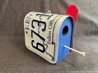Left-front view showing license plate sides, entry hole, perch, red flag
