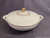 Front angled view of covered serving bowl showing lid, handles, gold finial