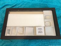 Front view of closed black shadow box showing glass front, interior foam and trays