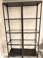 Front view of two identical black metal frame shelving units with glass shelves