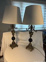 Front view showing both matching ornate gold-tone lamps with black orbs and cream shades