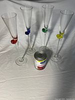 Four champagne flutes with colored heart accents beside soup can for scale