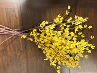 Group of bright yellow artificial forsythia stems laid on wooden surface