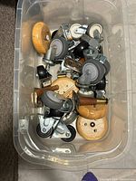Assorted casters and wooden feet inside clear bin