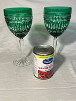 Two green cut stemmed wine glasses standing beside a can for scale