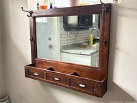 Full view of wooden mirror unit mounted on wall showing mirror, drawers, cubbies, and hooks