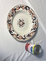 Top view of ornate ceramic serving plate beside standard can for scale