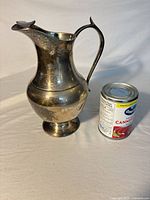 Side view of silver-plated pitcher beside can for scale, shows shape, handle, spout, tarnish