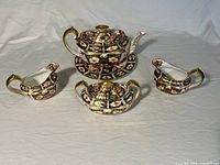 Front view of full tea set showing teapot on saucer, sugar bowl with lid and two creamers
