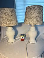 Two white ceramic table lamps with script shades beside a can for scale
