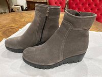 Lateral view of both boots showing suede upper, wedge sole, side zipper