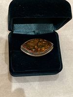 Front view of brooch in display box showing amber cabochon and silver frame