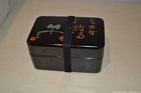 Closed black bento box secured with elastic band showing decorative lid.