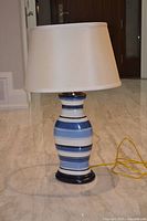 Full view of lamp showing striped ceramic base, shade, cord