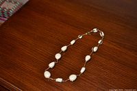 Full view of gold-tone chain necklace with white teardrop faux pearls on wooden surface