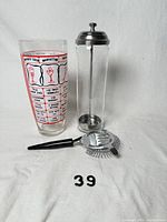 Front view of mixing glass, glass cylinder with plunger, and strainer