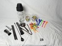 All items arranged on white cloth showing shaker, glasses, tools, straws, stirrers and picks