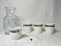 Six-piece lot laid out: four white mugs with blue band, milk glass creamer, clear duck carafe