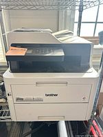 Front and side view of Brother MFC-L3750CDW printer on rack