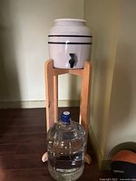 Ceramic dispenser on wood stand with glass jug below