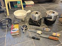Full lot overview: three fondue pots on stands, forks, ladle, boxed burner, support ring