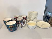 Group image showing all 14 pieces: 3 holiday mugs, 4 blue bowls, 6 cream reindeer bowls, 1 cream reindeer plate