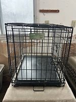 Front view of folded-up black wire dog crate showing label and plastic tray
