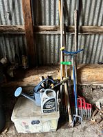 Group of long-handled tools, watering can, herbicide bottle on tote