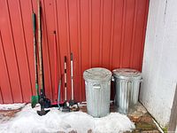 All five hand tools and two trash cans lined against red wall