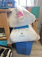 Two 5-lb fiberfill bags stacked on blue bin with additional plastic-wrapped fiberfill roll